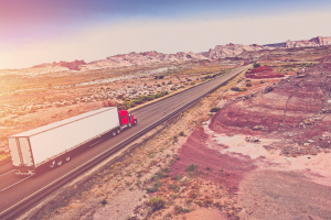 A semi-truck driving across a highway in the desert
